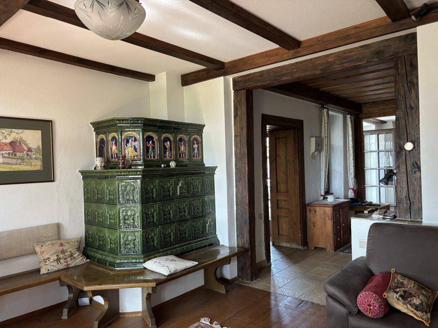 Gemütlicher Wohnbereich mit traditionellem Kachelofen, Holzbänken und sichtbaren Deckenbalken.