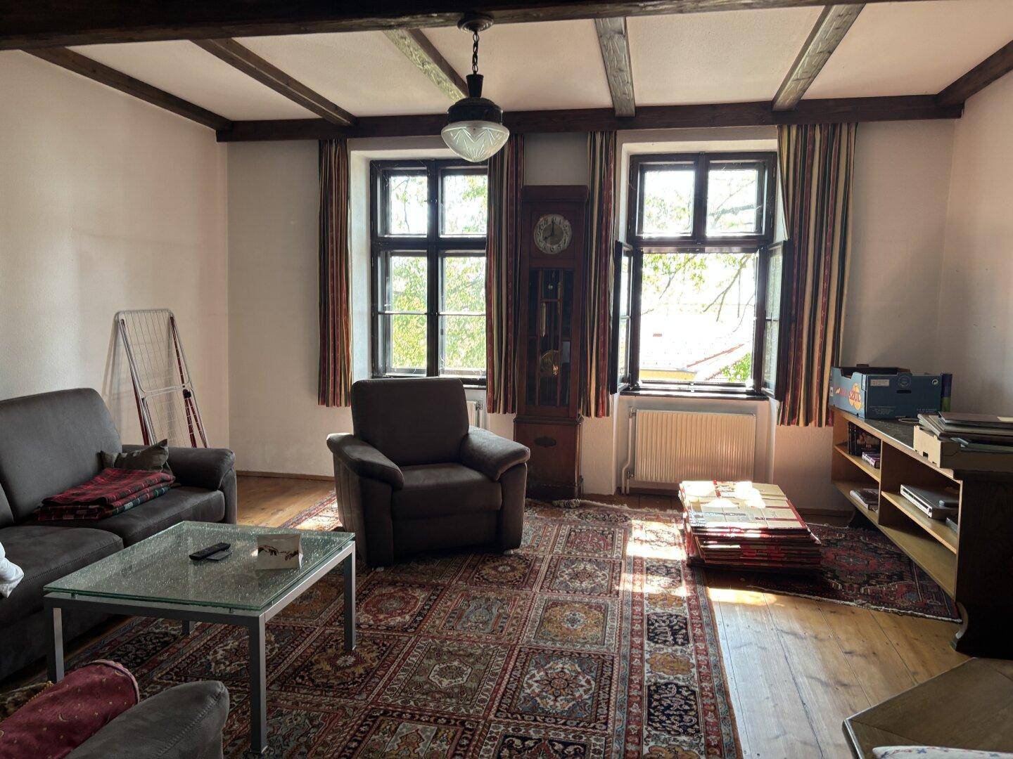 Geräumiges Wohnzimmer mit Holzboden, bequemen Sitzmöbeln und sichtbaren Deckenbalken.