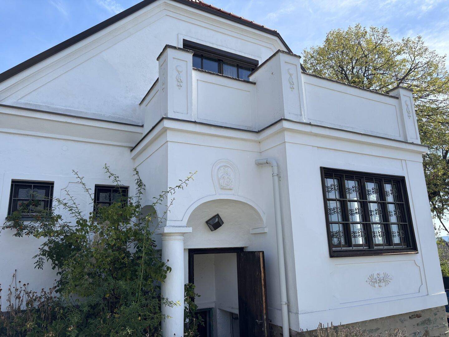 Weiße Hausfassade mit dekorativen Elementen und einem überdachten Eingangsbereich.