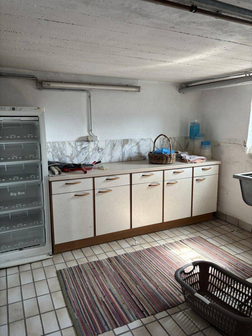 Praktischer Hauswirtschaftsraum im Keller mit Schränken, Gefrierschrank und Fliesenboden.