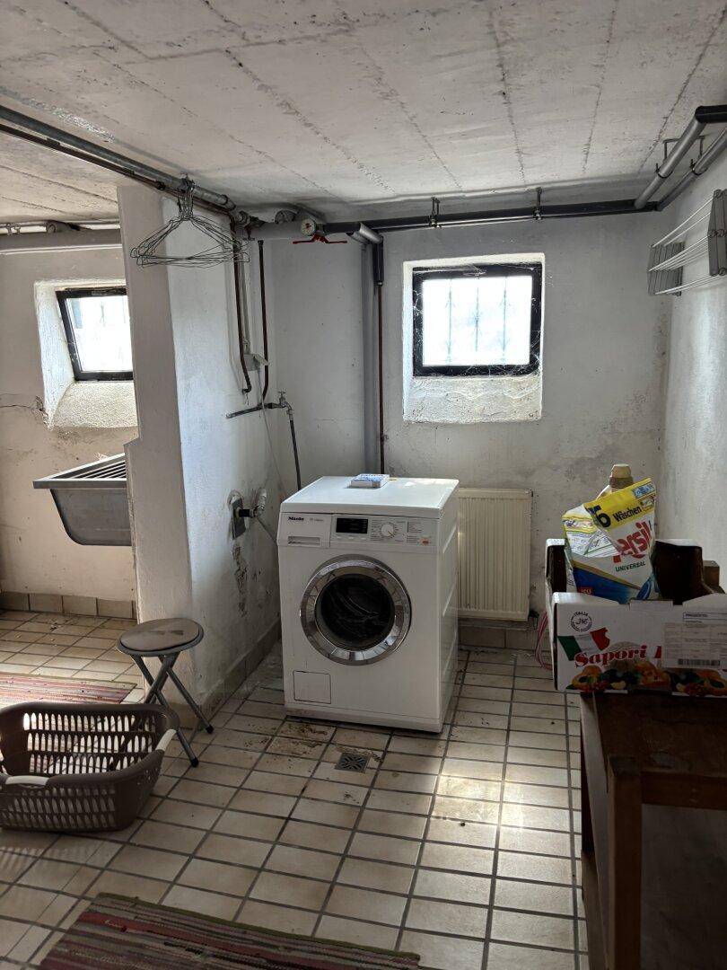 Waschküche im Keller mit Waschmaschine, Waschbecken und Fliesenboden.