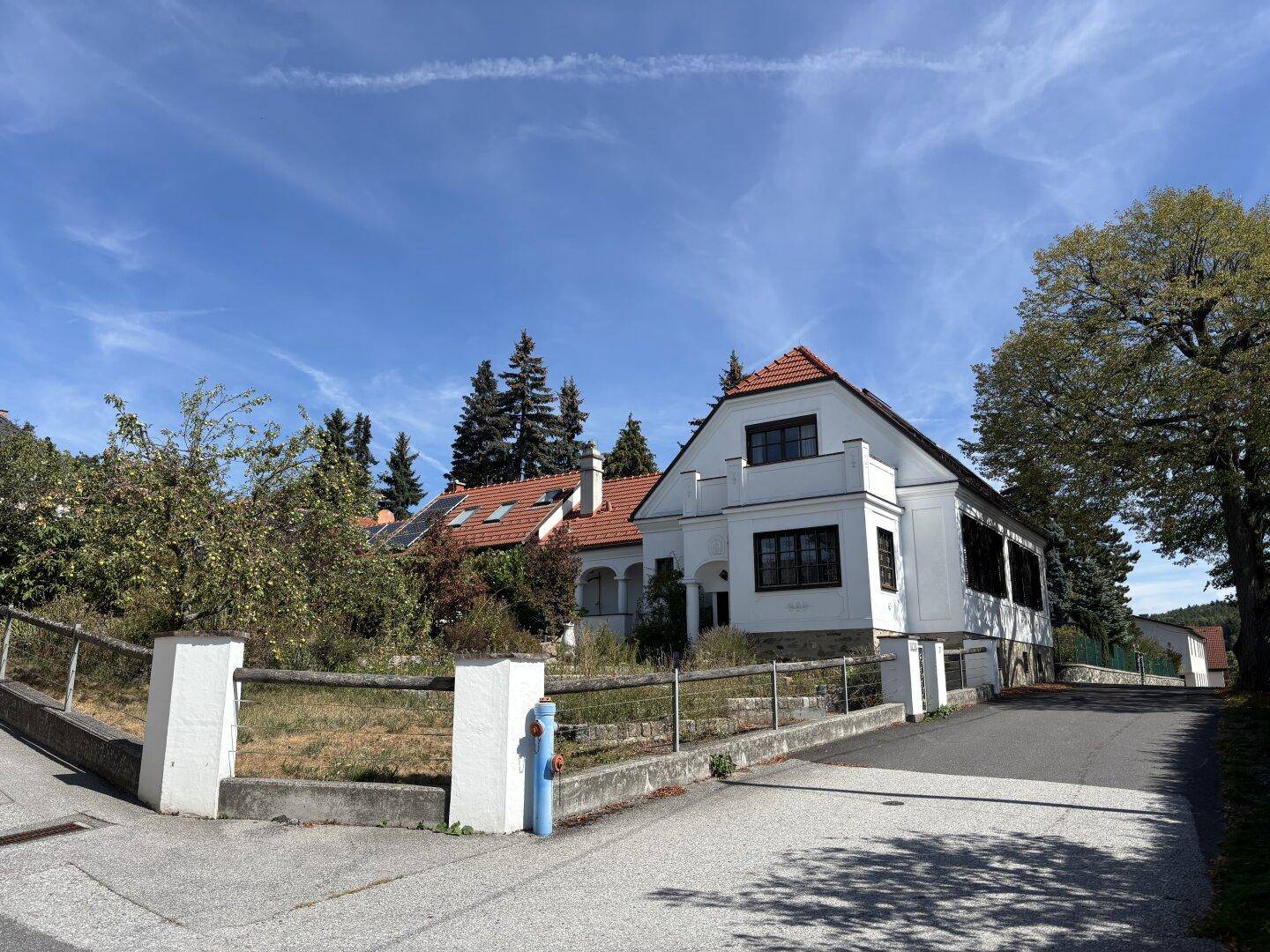 Charmantes weißes Haus mit Ziegeldach und weitläufigem Grundstück, umgeben von Bäumen und Natur.