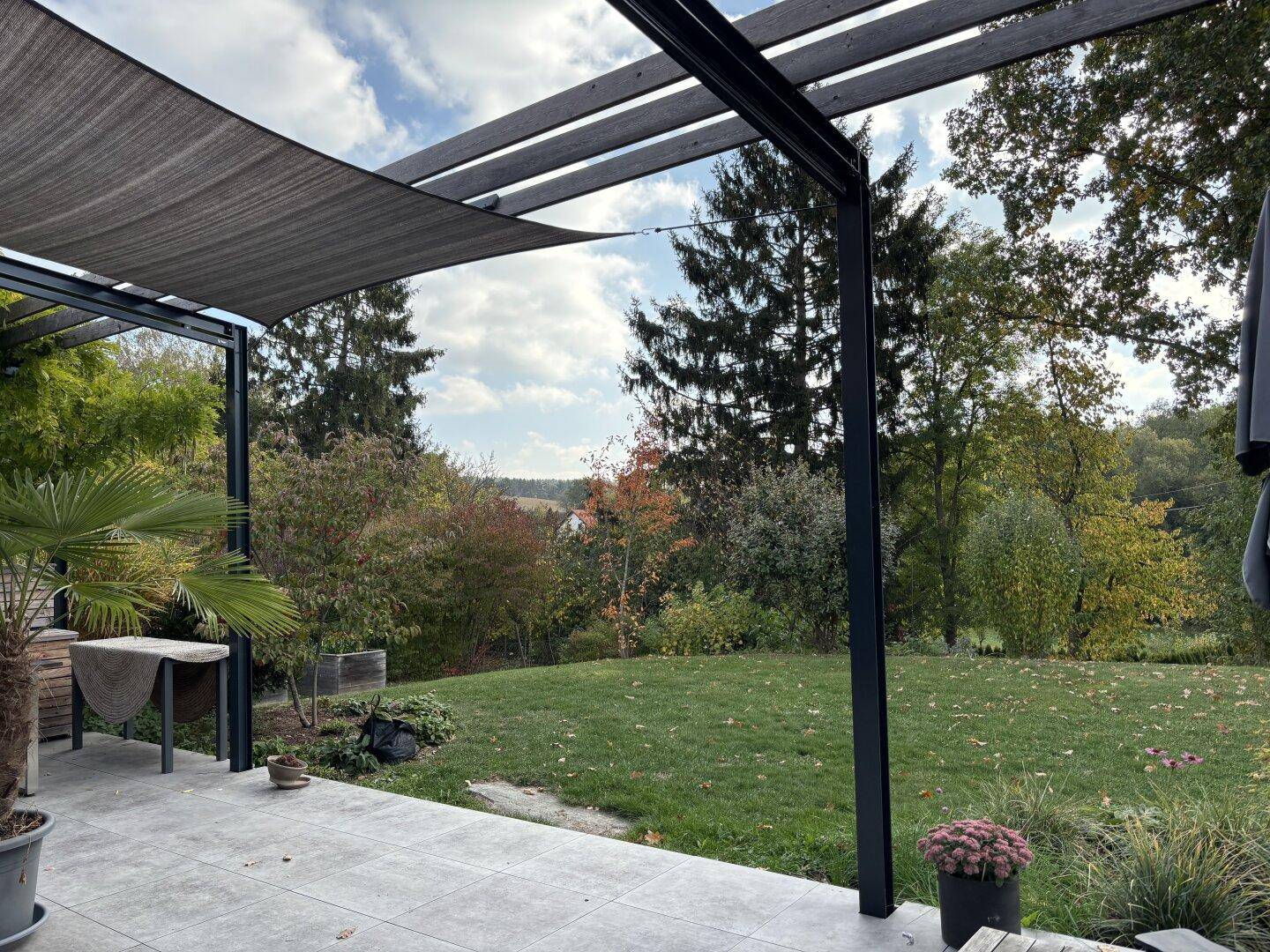 Entspannende Terrasse mit Beschattung, einer Palme und weitem Blick über den Garten und die Landschaft.