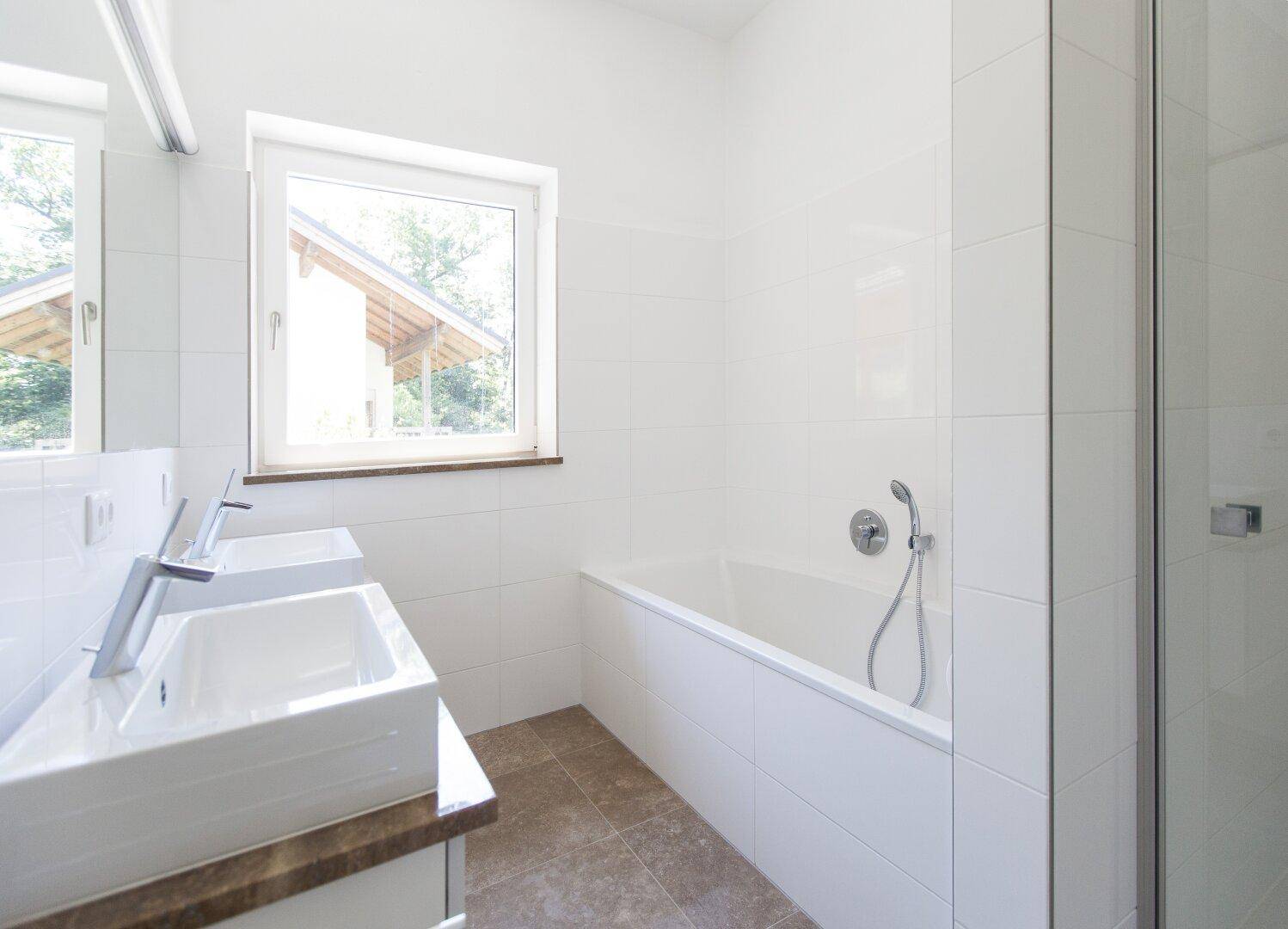 Modernes Badezimmer mit Doppelwaschbecken, Badewanne und Fenster für natürliches Tageslicht.