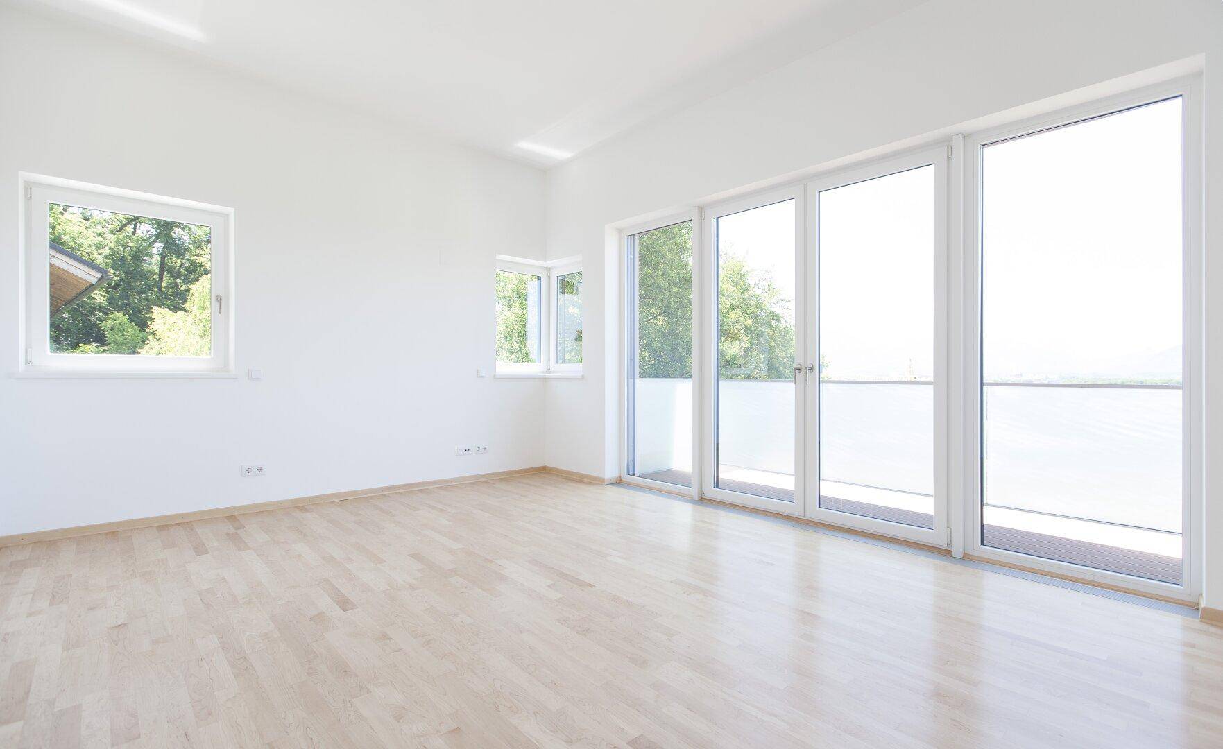 Lichtdurchfluteter Wohnraum mit Holzboden und weitem Ausblick durch große Fensterfronten.