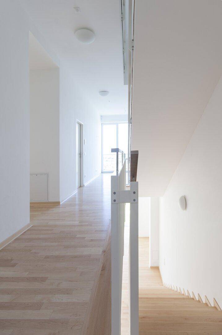 Heller Flur im Obergeschoss mit Holzboden und Blick auf die offene Holztreppe.