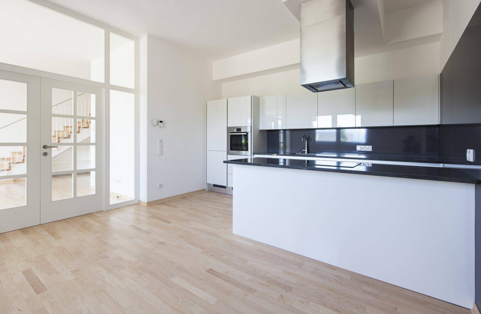 Helle, moderne Küche mit Kochinsel, weißen Hochglanzfronten und hellem Holzboden in offener Gestaltung.