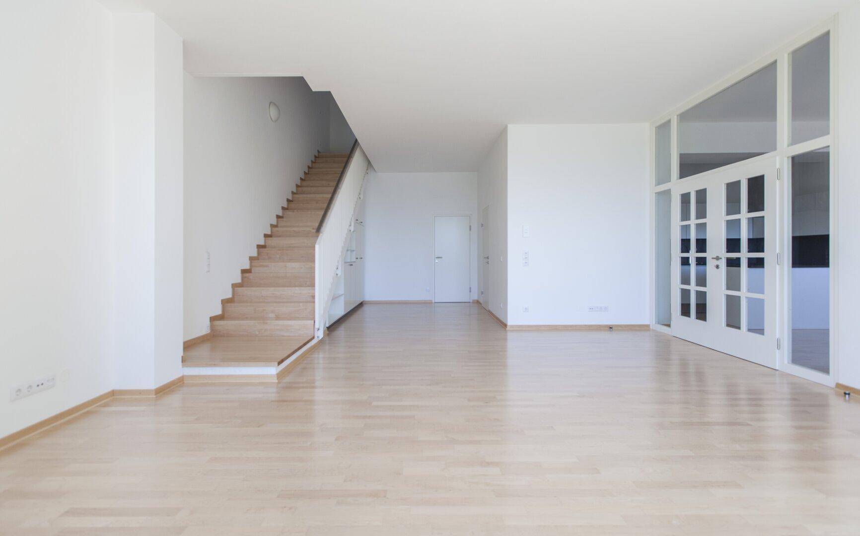 Geräumiger, heller Wohnbereich mit Holzboden und offenem Zugang zu einer Holztreppe.