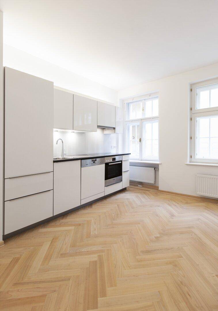 Neue, helle Küche mit modernen Schränken, integrierten Geräten und Fischgrätparkettboden.