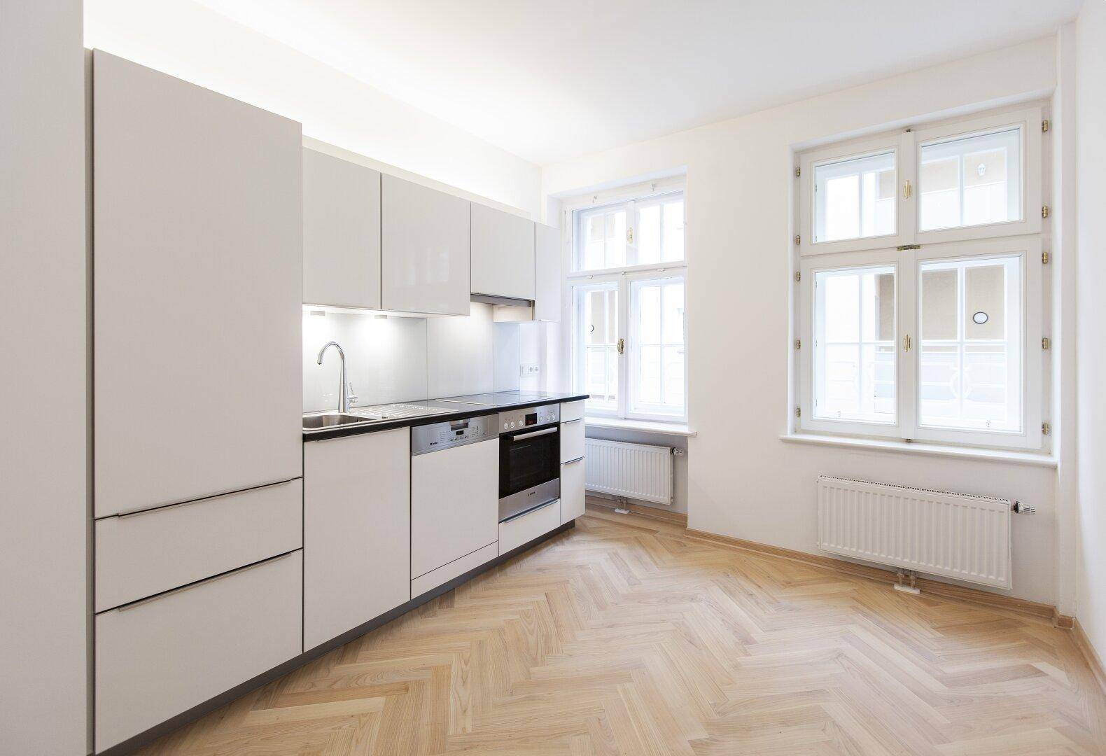 Moderne Einbauküche mit hellgrauen Fronten, integrierten Geräten und Fischgrätparkett.