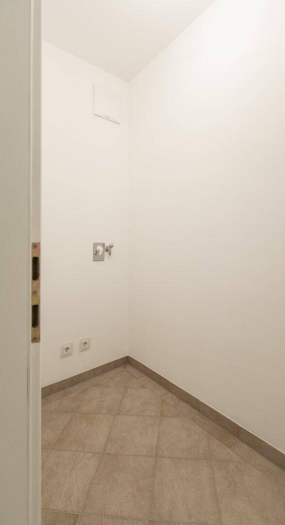 Leerer Hauswirtschaftsraum mit Fliesenboden und Anschlüssen, ideal für Waschmaschine.