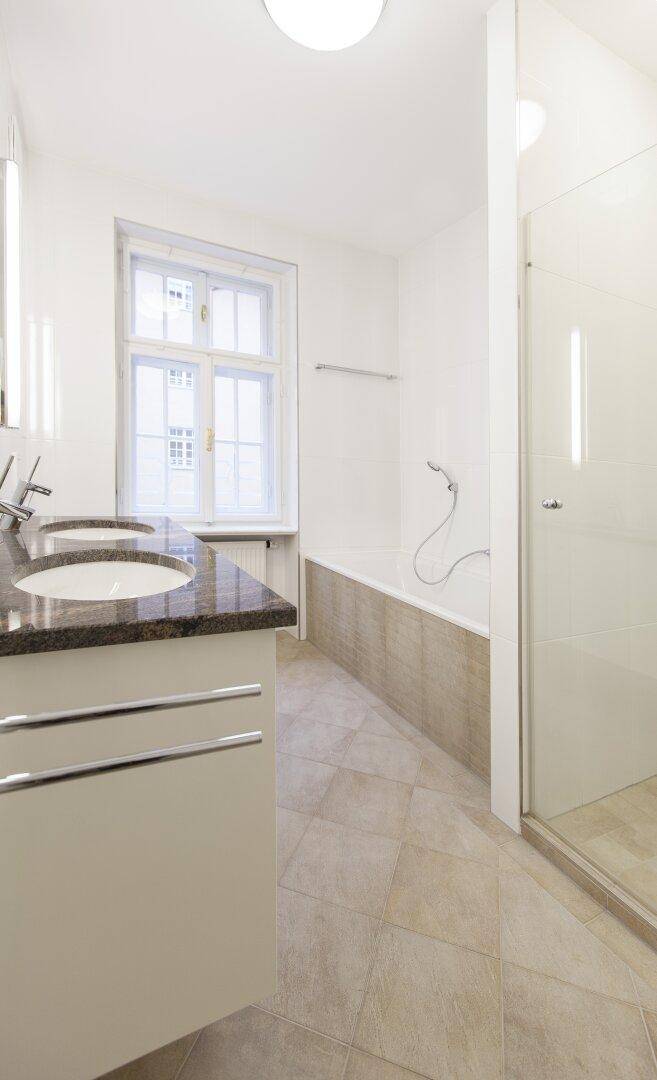 Modernes Badezimmer mit Doppelwaschbecken, Badewanne und Duschkabine, hell gefliest.
