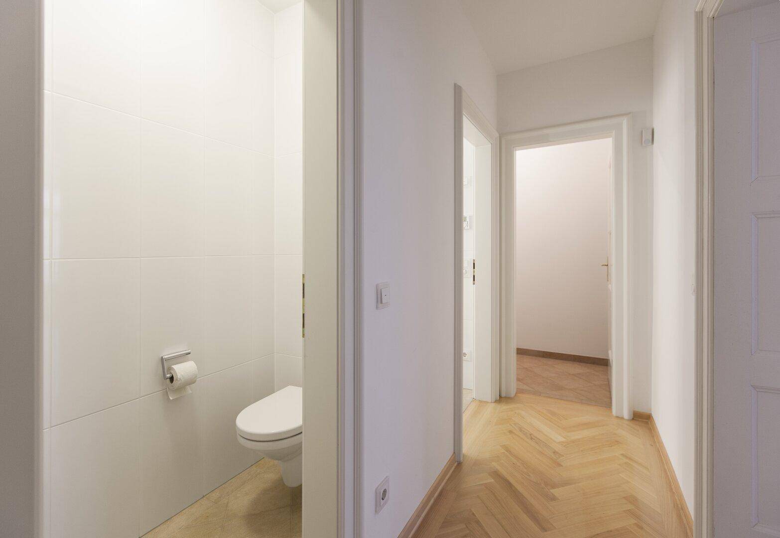 Modernes Gäste-WC mit wandhängender Toilette und weißen Fliesen.