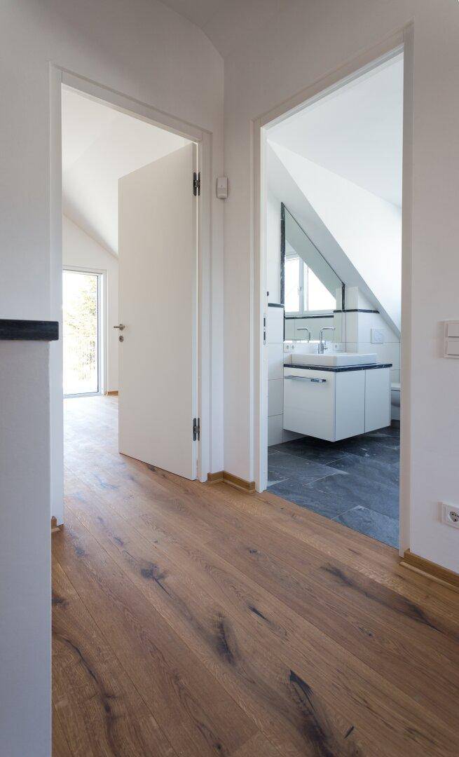 Heller Flur mit Holzboden, der zu einem modernen Badezimmer mit Dachschräge führt.