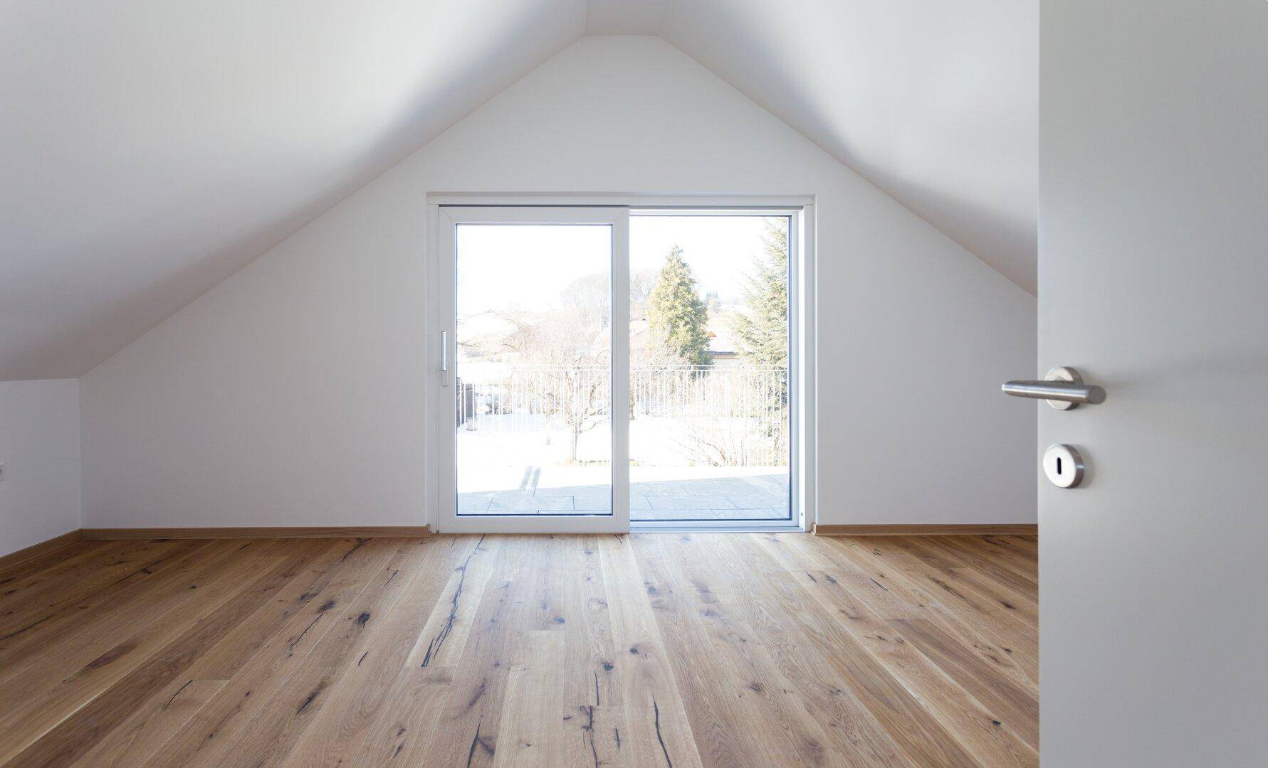 Geräumiges Schlafzimmer im Dachgeschoss mit Holzboden und Zugang zu einem Balkon.