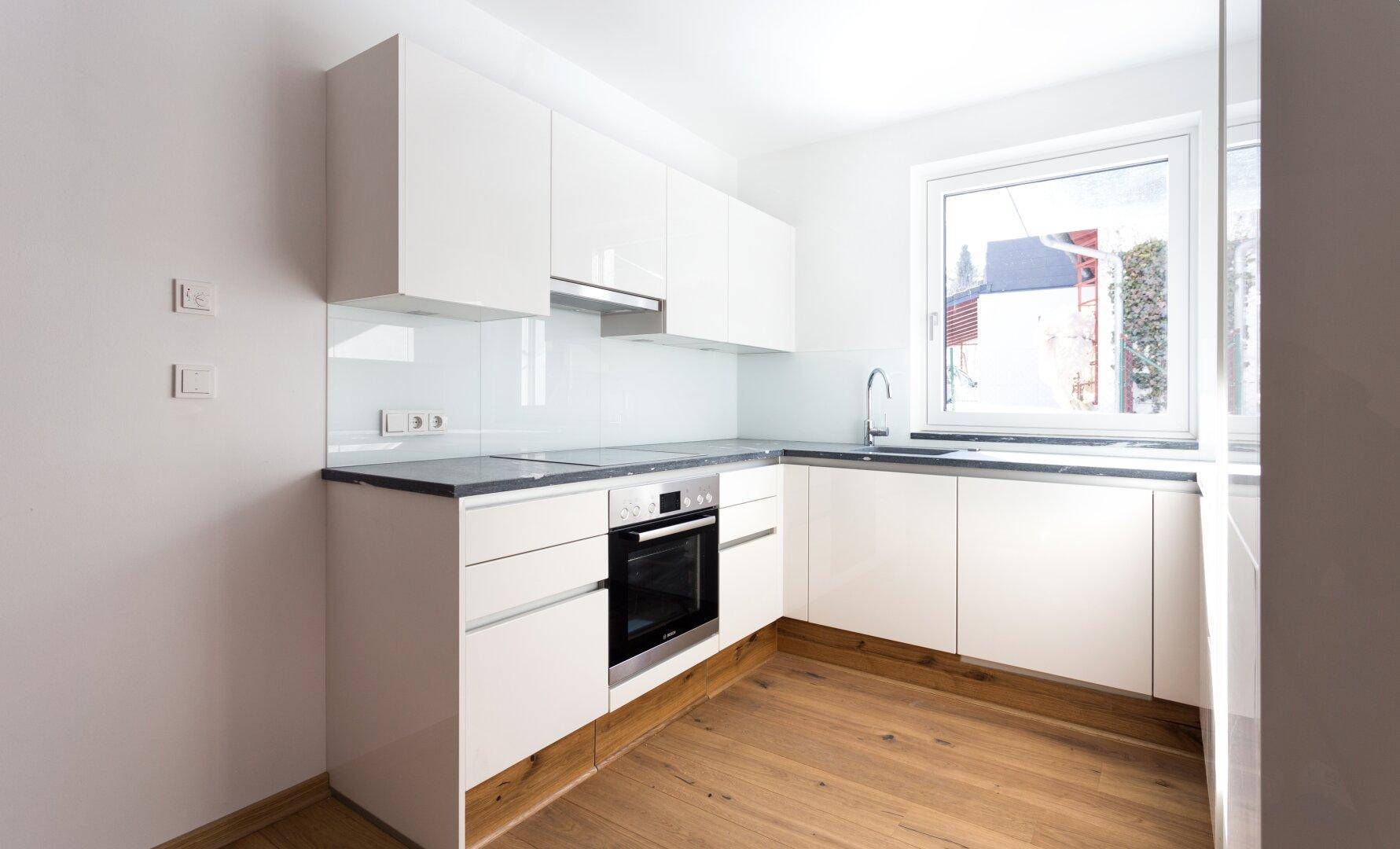 Moderne Einbauküche in Weiß mit glänzenden Fronten, integrierten Geräten und Fenster.
