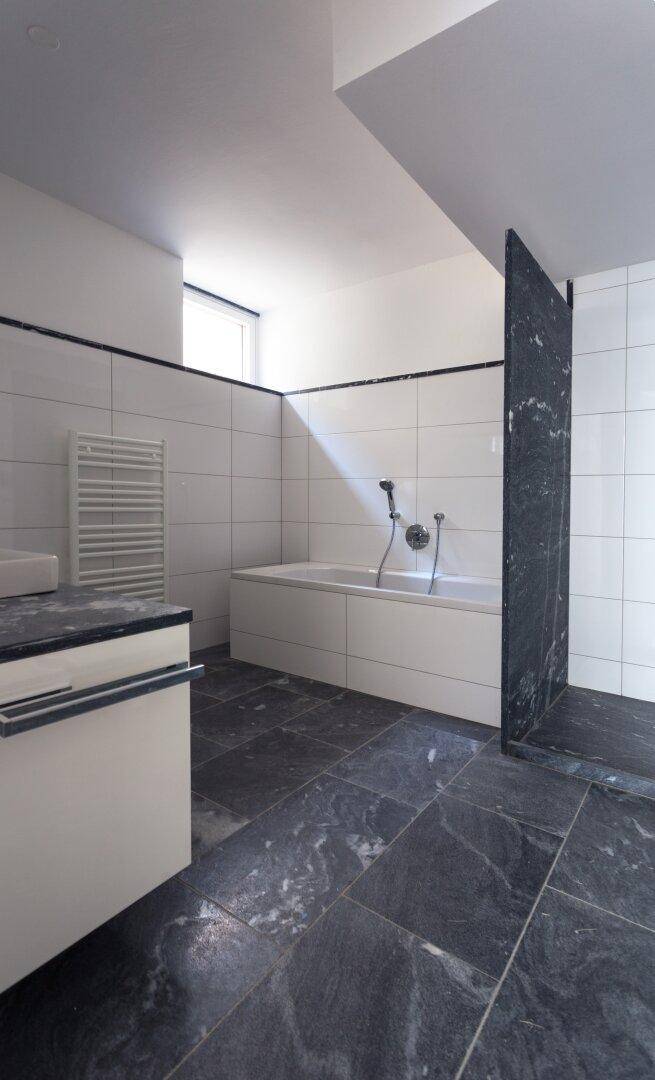 Modernes Badezimmer mit dunklen Fliesen, Badewanne und beheiztem Handtuchhalter.