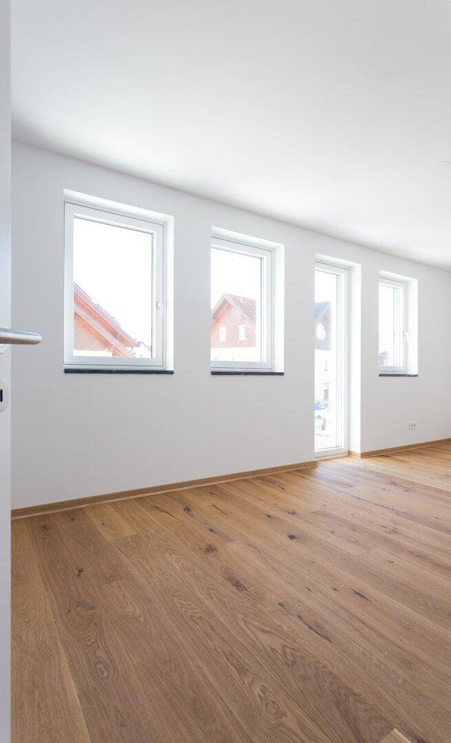 Heller Raum mit Holzboden und mehreren Fenstern, die viel Tageslicht hereinlassen.