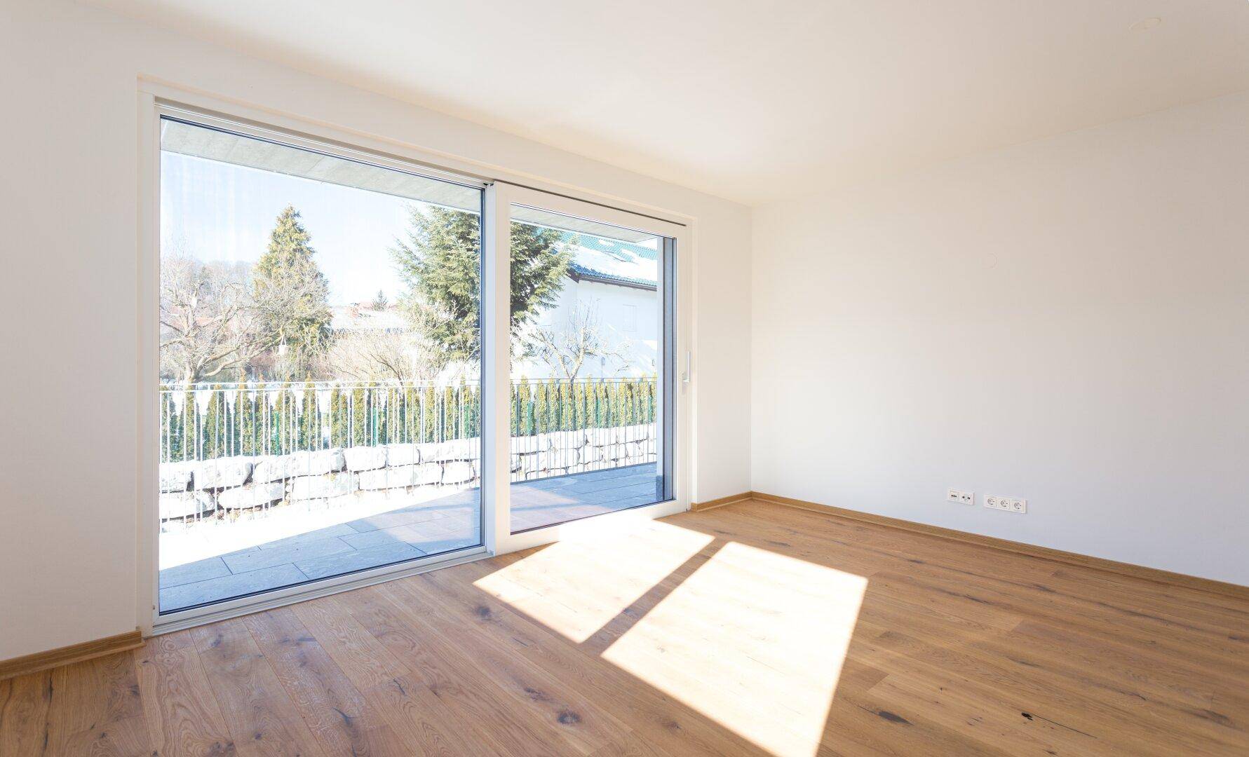 Lichtdurchfluteter Raum mit Holzboden und großer Schiebetür, die Zugang zu einer Terrasse bietet.