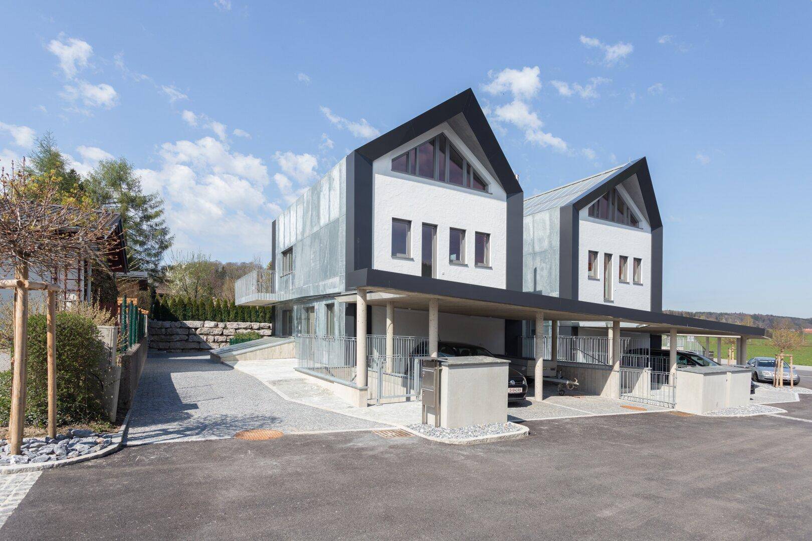Moderne Reihenhäuser mit Carports und gepflasterter Zufahrt in sonniger Umgebung.