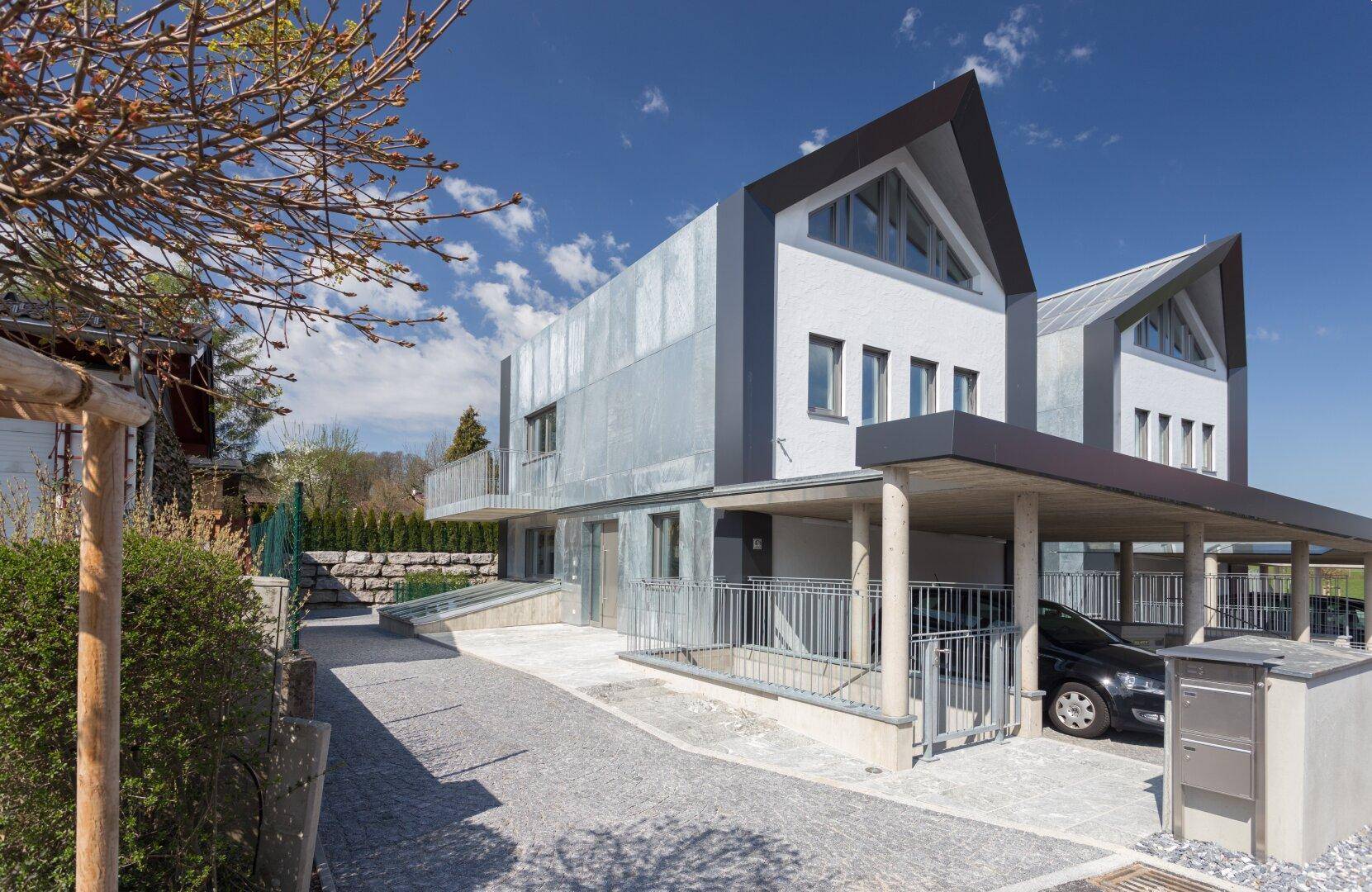 Moderne Reihenhäuser mit Carports und gepflasterter Zufahrt unter strahlend blauem Himmel.
