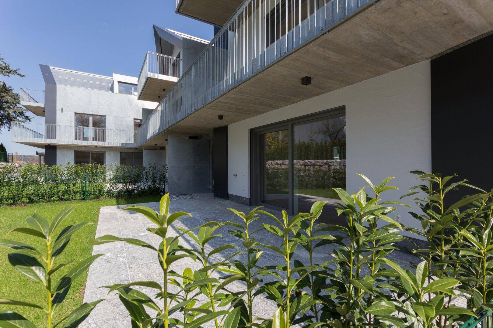 Große Steinterrasse mit Zugang zum Garten und Blick auf die moderne Architektur.