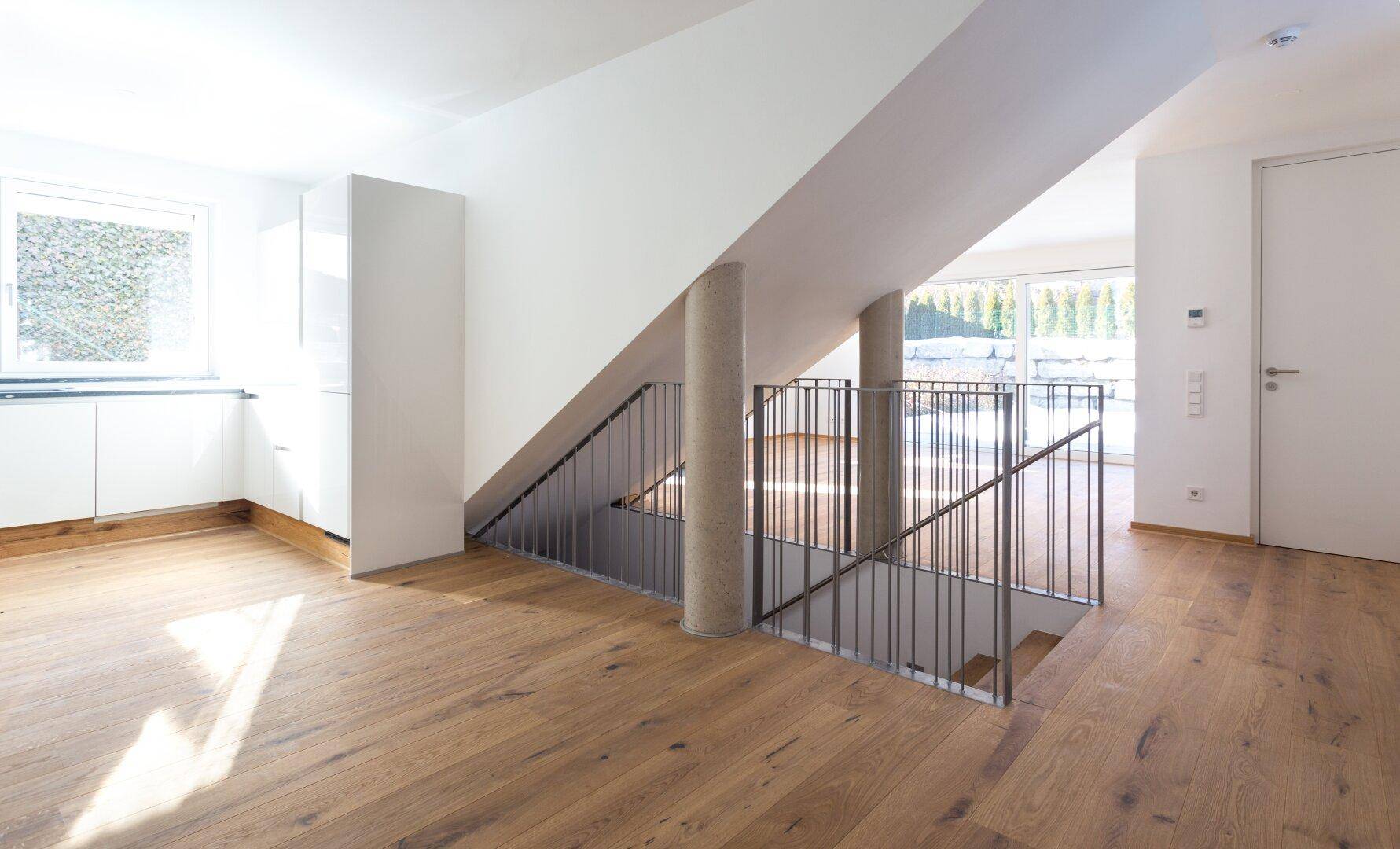 Offener Wohnbereich mit Holzboden, moderner Küche und Treppe zu den oberen Etagen.