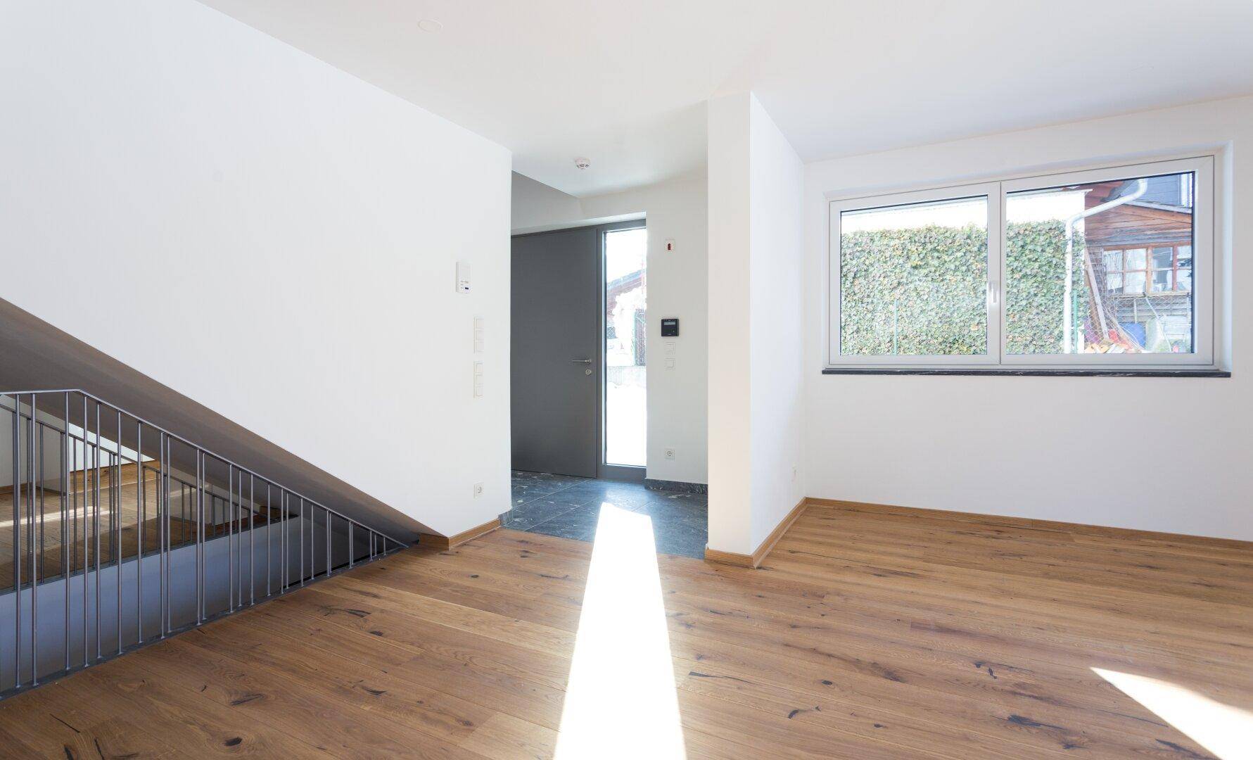 Heller Eingangsbereich mit Holzboden, Treppe und großem Fenster, das viel Licht spendet.