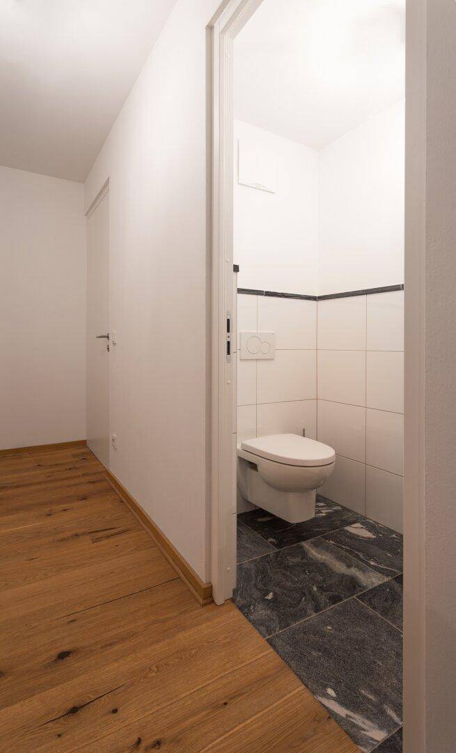 Kleines Gäste-WC mit Wand-WC, dunklen Fliesen und weißer Wandgestaltung.