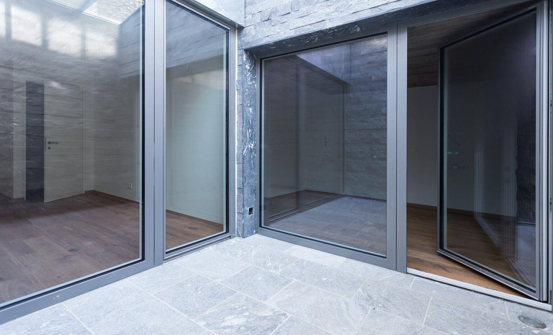 Heller Innenhof mit Steinfliesen und großen Glasfronten, die zu den Wohnräumen führen.