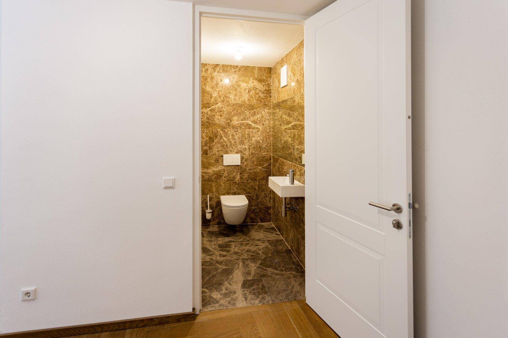 Modernes Gäste-WC mit Marmorfliesen, wandhängendem WC und kleinem Waschbecken.