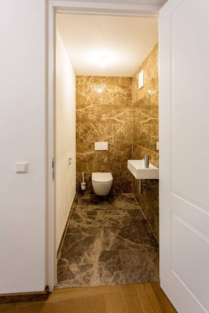 Modernes Gäste-WC mit Marmorfliesen, wandhängendem WC und kleinem Waschbecken.