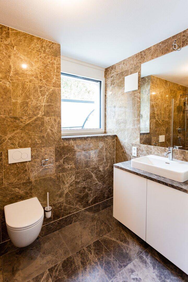 Elegantes Badezimmer mit braunen Marmorfliesen, Waschtisch und Fenster.