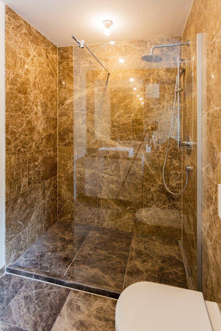 Geräumige begehbare Dusche mit Glasabtrennung und luxuriösen Marmorfliesen.