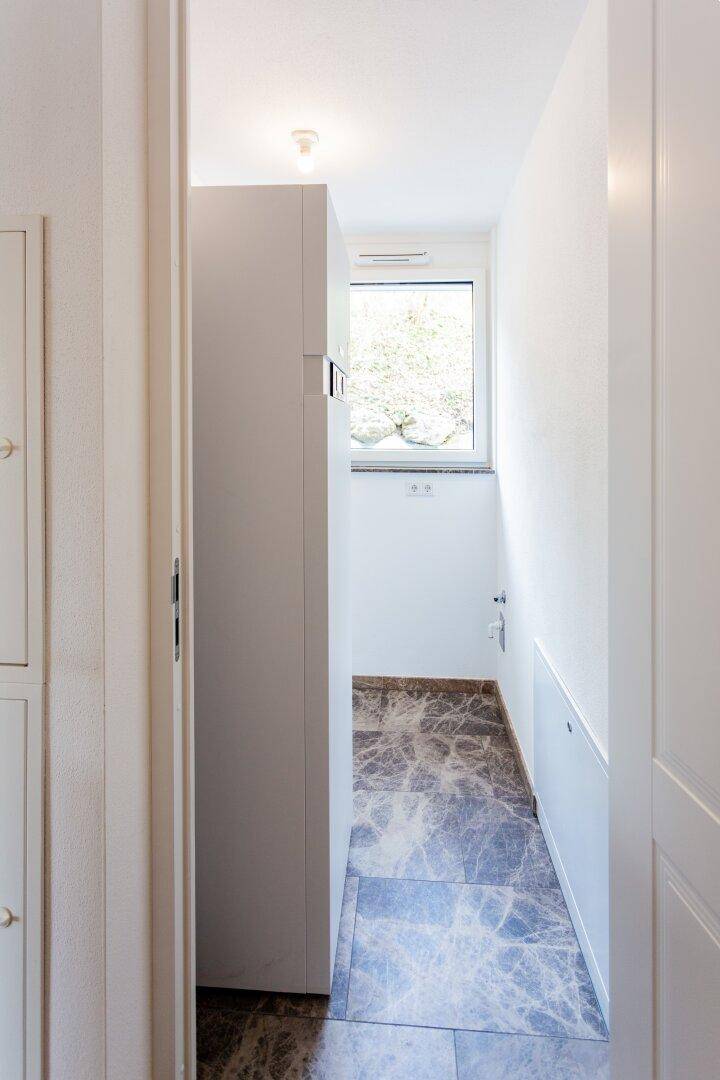 Schmaler Hauswirtschaftsraum mit Fenster und gefliestem Boden, ideal für Waschmaschine.