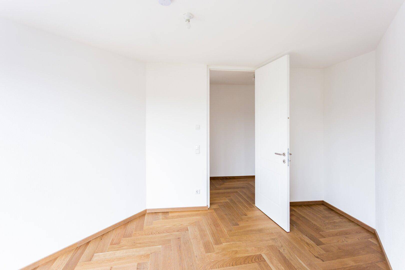 Leeres Zimmer mit Fischgrätparkett und weiß gestrichenen Wänden, bereit zum Einzug.