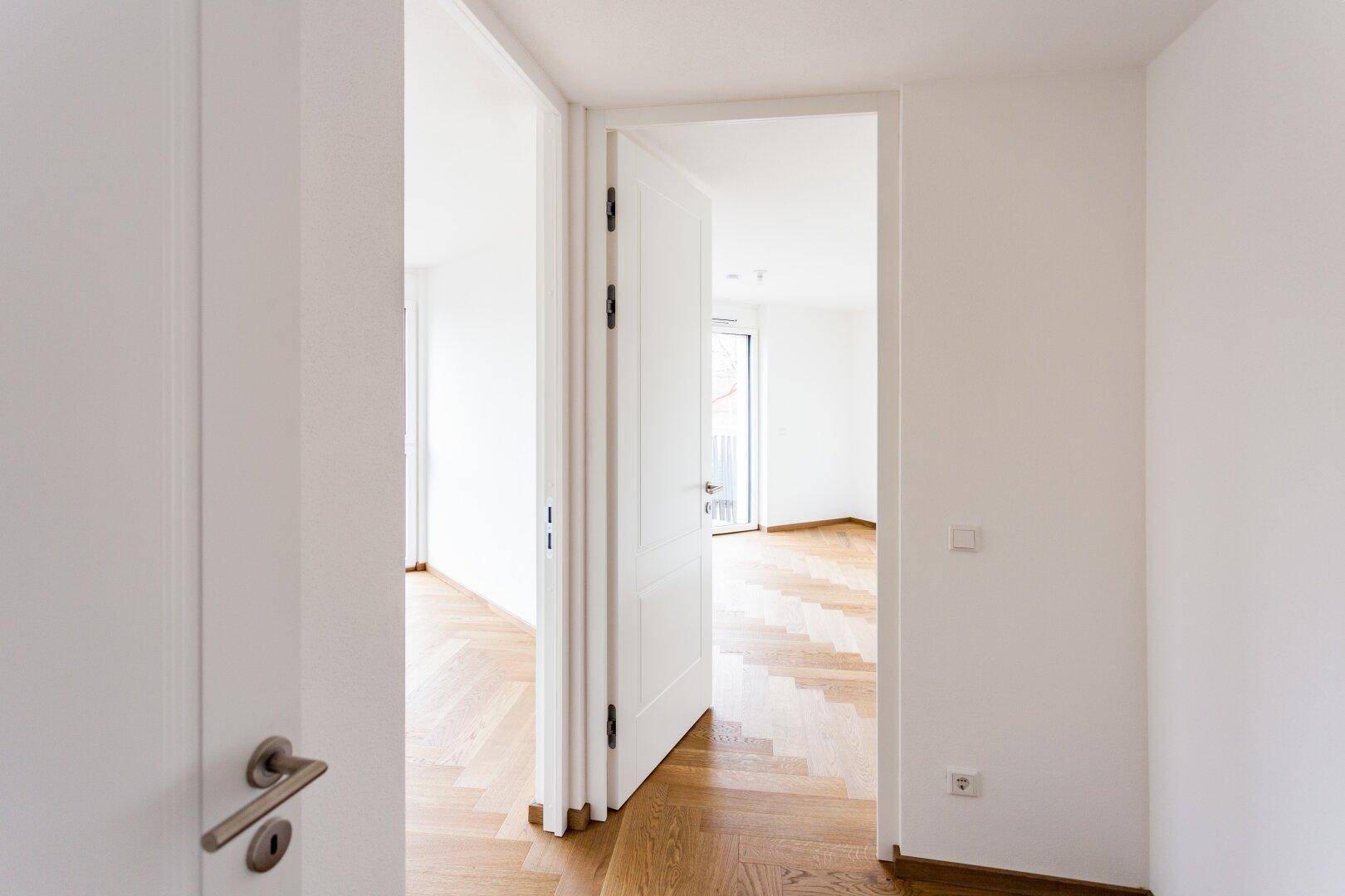Heller Durchgangsbereich mit Fischgrätparkett, der zu einem weiteren Zimmer führt.