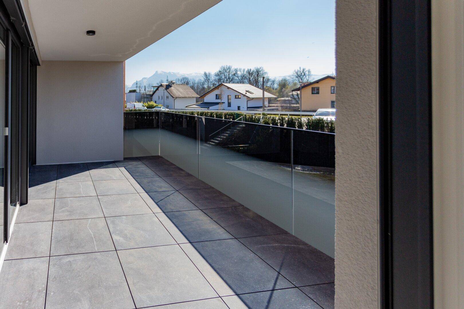 Heller Balkon mit Fliesenboden und Glasbrüstung, mit Fernblick auf die Berge.