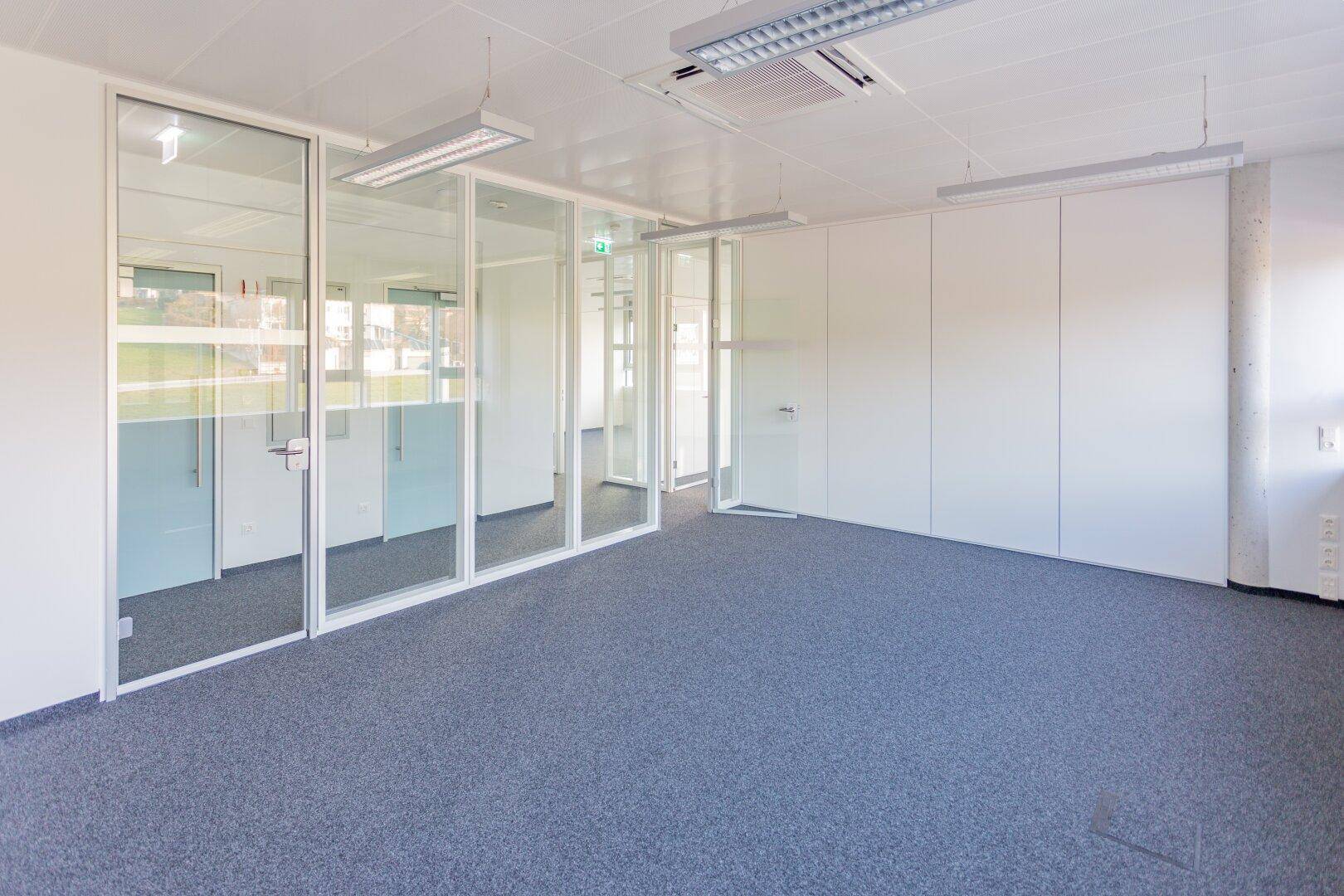 Großes, helles Büro mit Teppichboden, Glaswänden und weißer Decke, ideal für flexible Arbeitsbereiche.