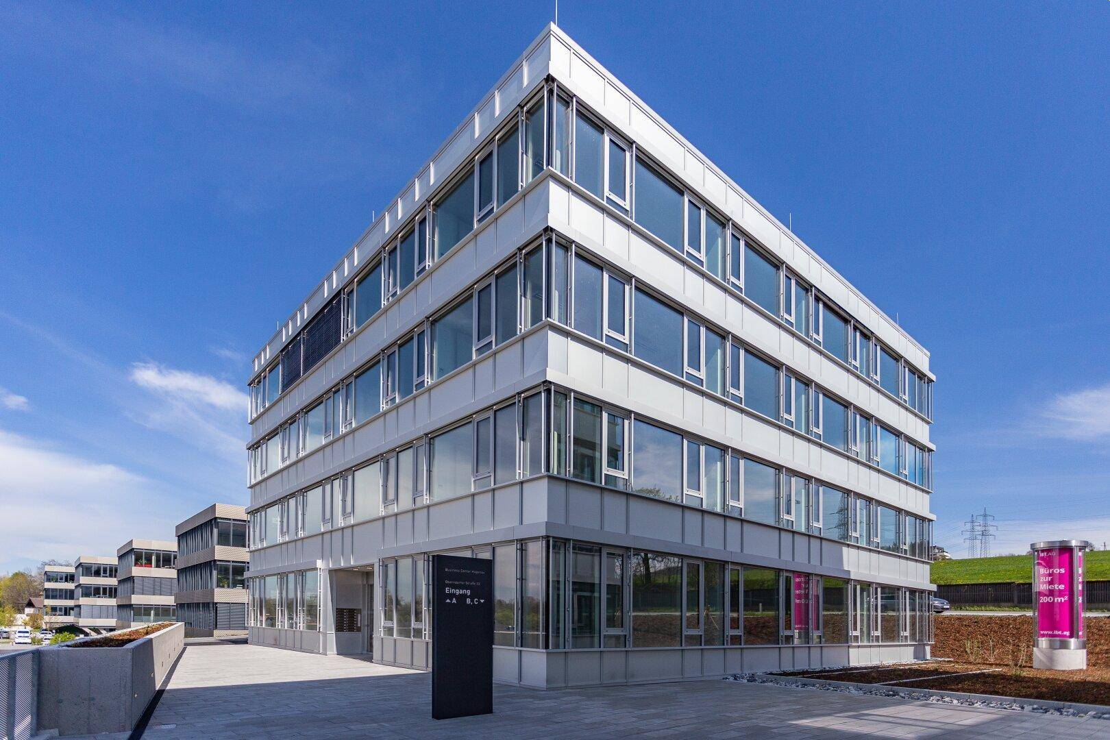 Modernes Bürogebäude mit Glasfassade und klaren Linien unter blauem Himmel.