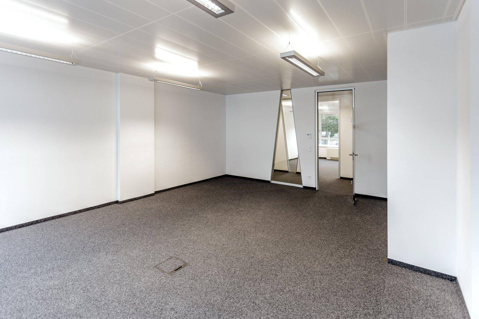 Leeres Büro mit Teppichboden und einer Tür, die zu weiteren Räumen führt, ideal für flexible Nutzung.