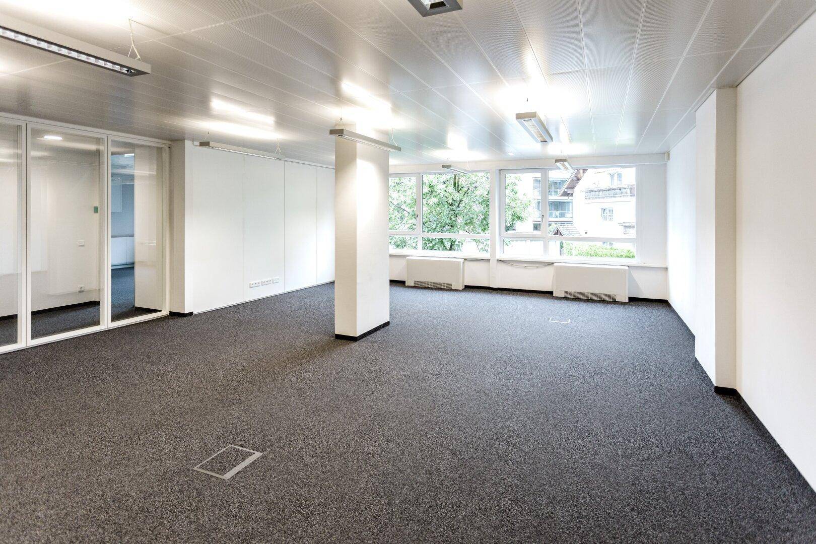 Großes, leeres Büro mit Teppichboden, Säulen und Glaswänden, das vielseitige Gestaltungsmöglichkeiten bietet.
