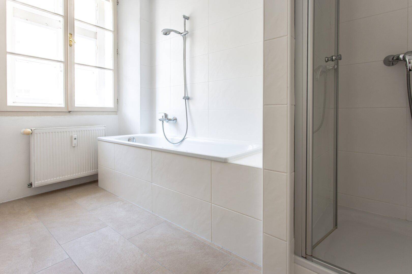 Badezimmer mit Badewanne, Duschvorrichtung und separater Duschkabine, hell gefliest.