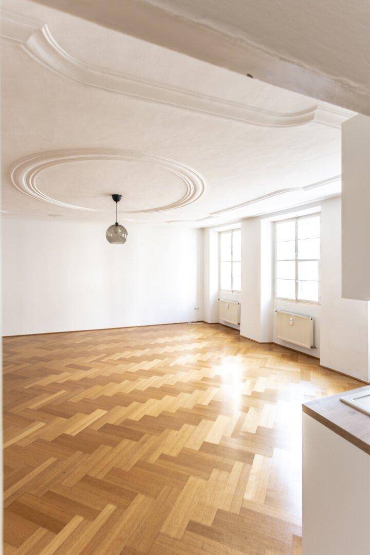 Geräumiges Zimmer mit Fischgrätparkett, Stuckdecke und großen Fenstern für viel Tageslicht.