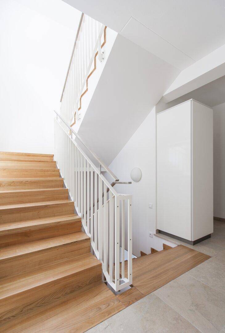 Elegante Holztreppe mit weißem Geländer, die die verschiedenen Ebenen verbindet.