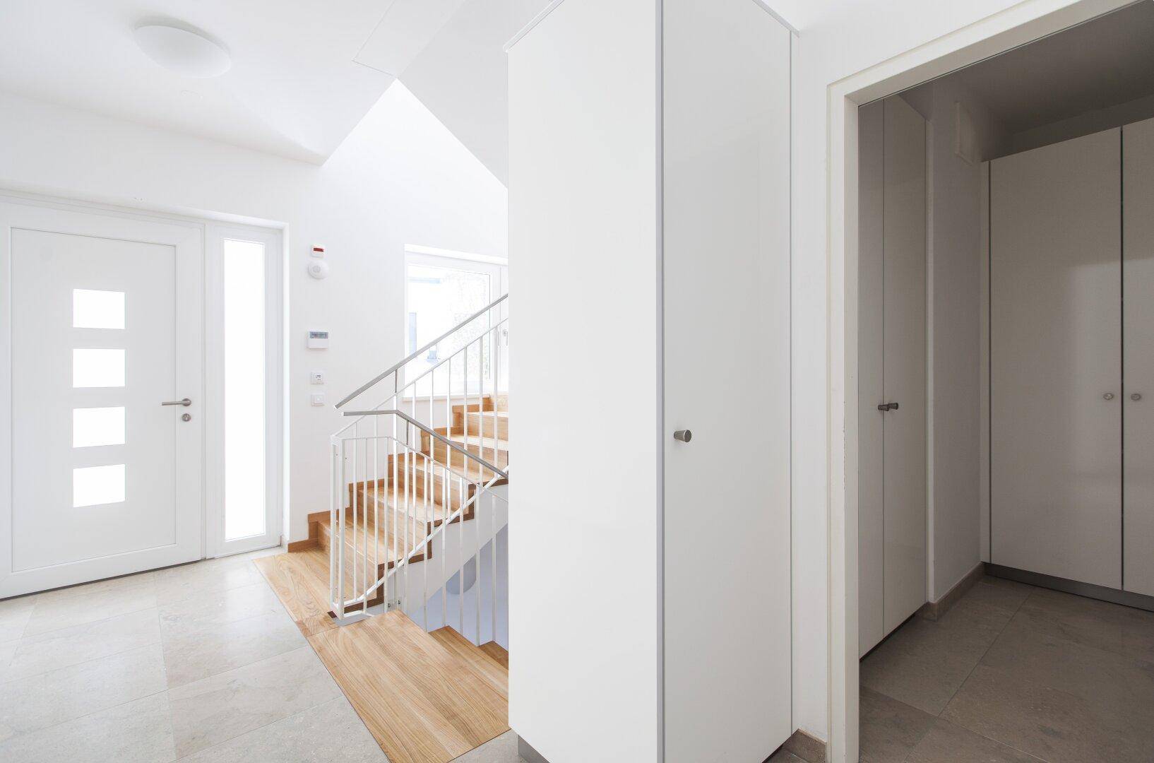 Geräumiger Flur mit Eingangstür, Einbauschränken und Blick auf die Holztreppe.