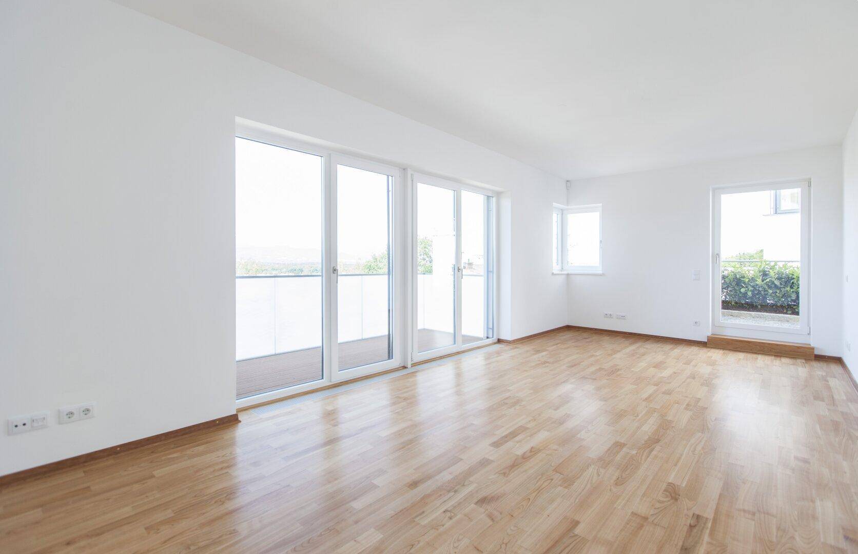 Heller Wohnraum mit Holzboden, großen Schiebetüren und Zugang zu einer Außenterrasse.