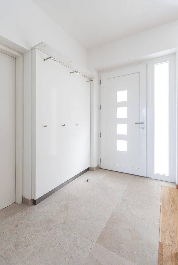 Heller Eingangsbereich mit Fliesenboden, Garderobe und moderner Eingangstür.