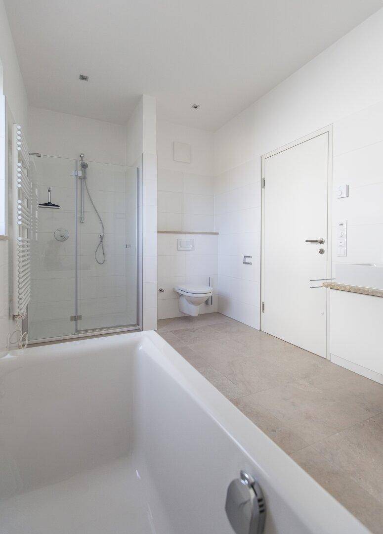 Modernes Badezimmer mit Badewanne, Dusche, Wand-WC und beheiztem Handtuchhalter.