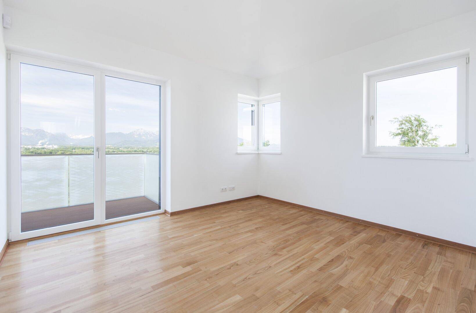 Helles Schlafzimmer mit Holzboden, großen Fenstern und weitem Blick auf die Landschaft.
